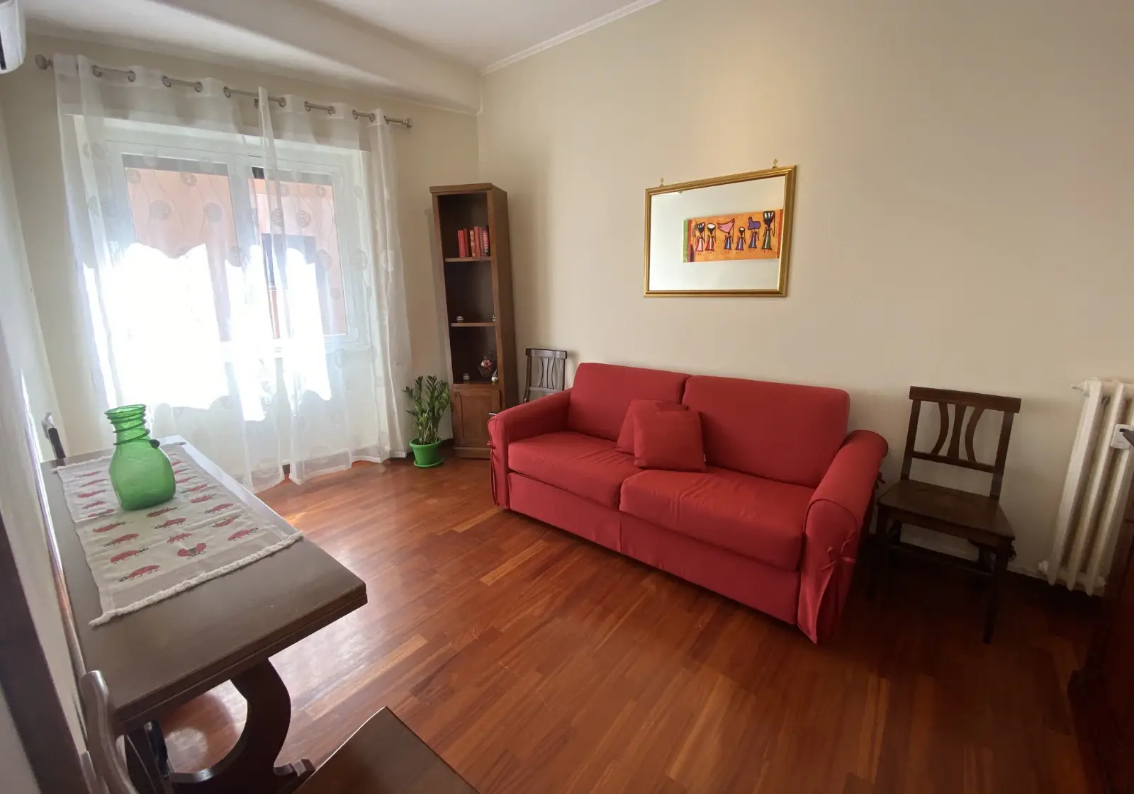 Jasny salon z czerwoną rozkładaną sofą i parkietem